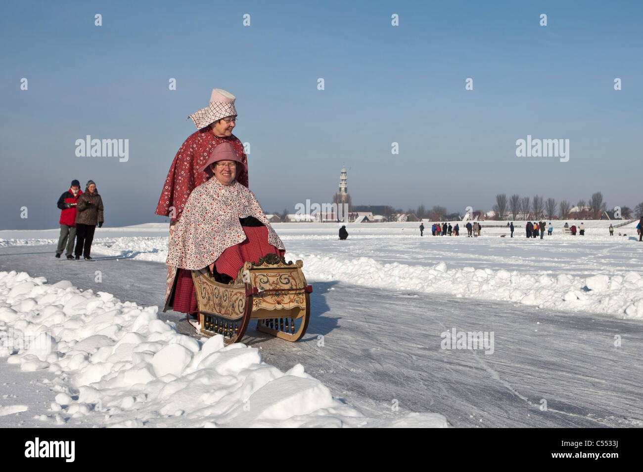 I Paesi Bassi, Hindeloopen, capitale olandese di pattinaggio di cultura. Le donne in costume tradizionale con lo slittino su ghiaccio. Foto Stock