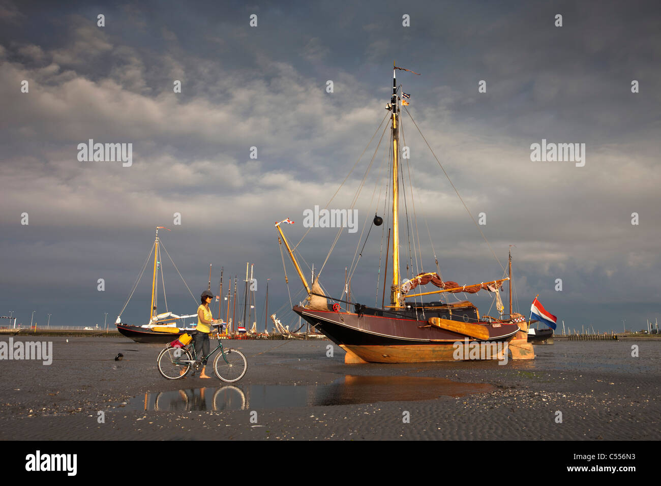 I Paesi Bassi, il Nes Ameland, Isola, appartenente al mare di Wadden Islands. Imbarcazione a vela sulla piana di fango nel porto. Donna e bicicletta. Foto Stock