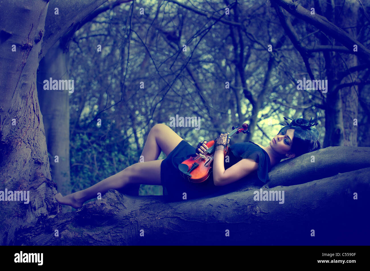 Triste donna con violino giacente su un tronco di albero Foto Stock