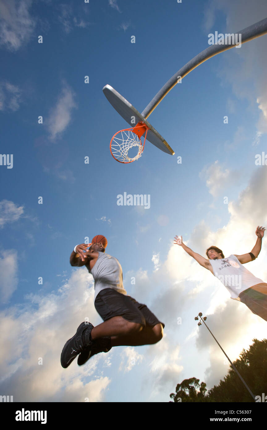 Punteggio maschio all'aperto durante il gioco del basket, inclinazione verso l'alto verso il traguardo Foto Stock