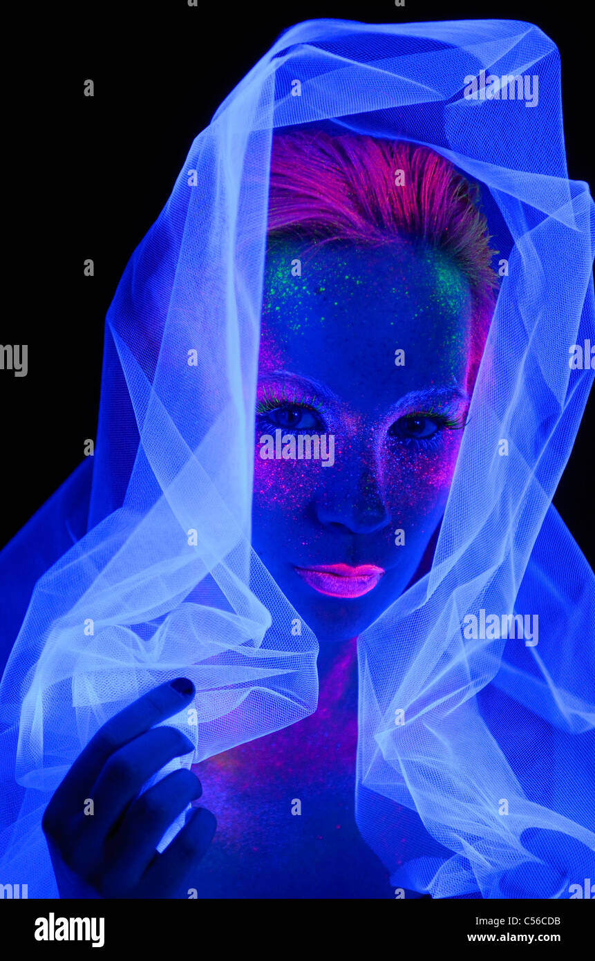 Viso di donna al buio con vernice fluorescente trucco tenendo un bianco  velo sotto il blu profondo delle luci di colore nero Foto stock - Alamy