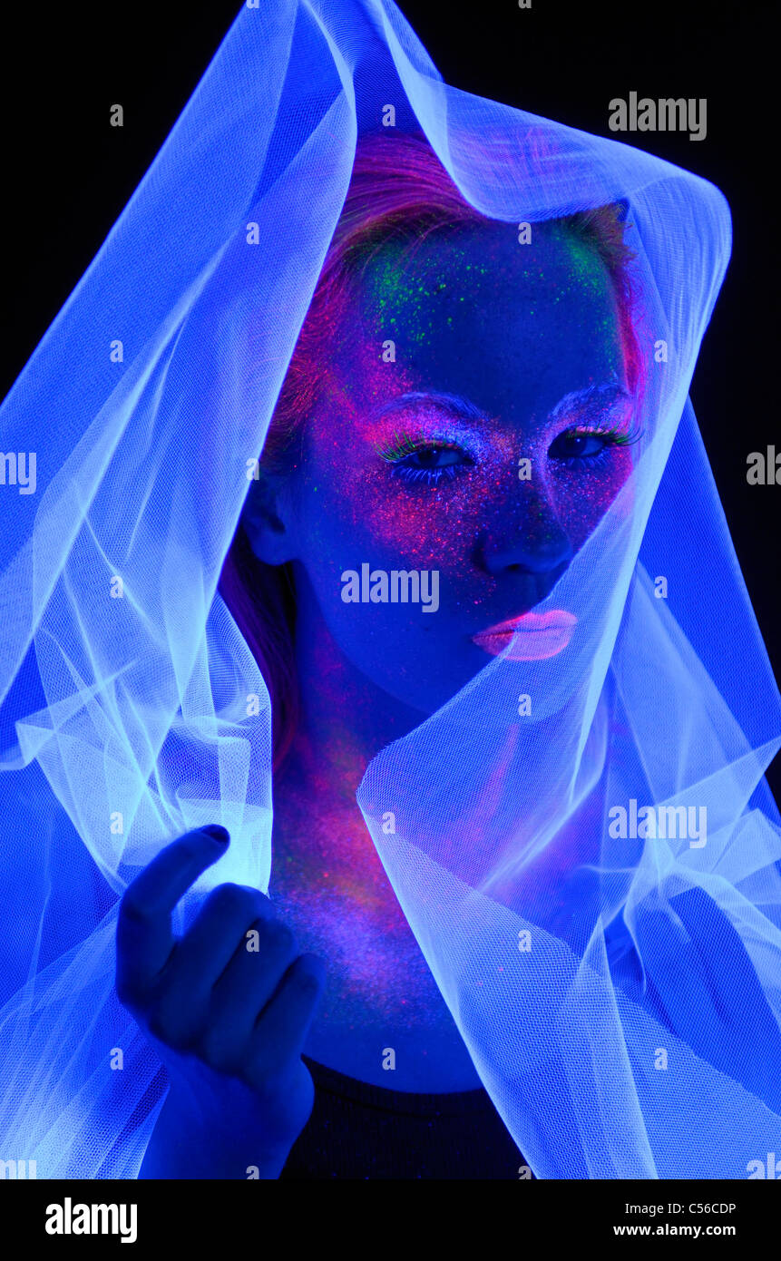 Viso di donna al buio con vernice fluorescente trucco dietro un velo bianco sotto le luci di colore nero Foto Stock