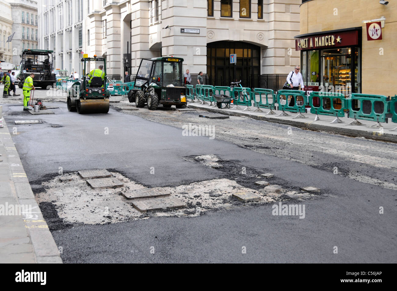 Street scene Road works macchine operatrici & lavoro in corso di ripavimentazione fuori strada asfaltata in City of London Manhole scoperto copre Inghilterra UK Foto Stock