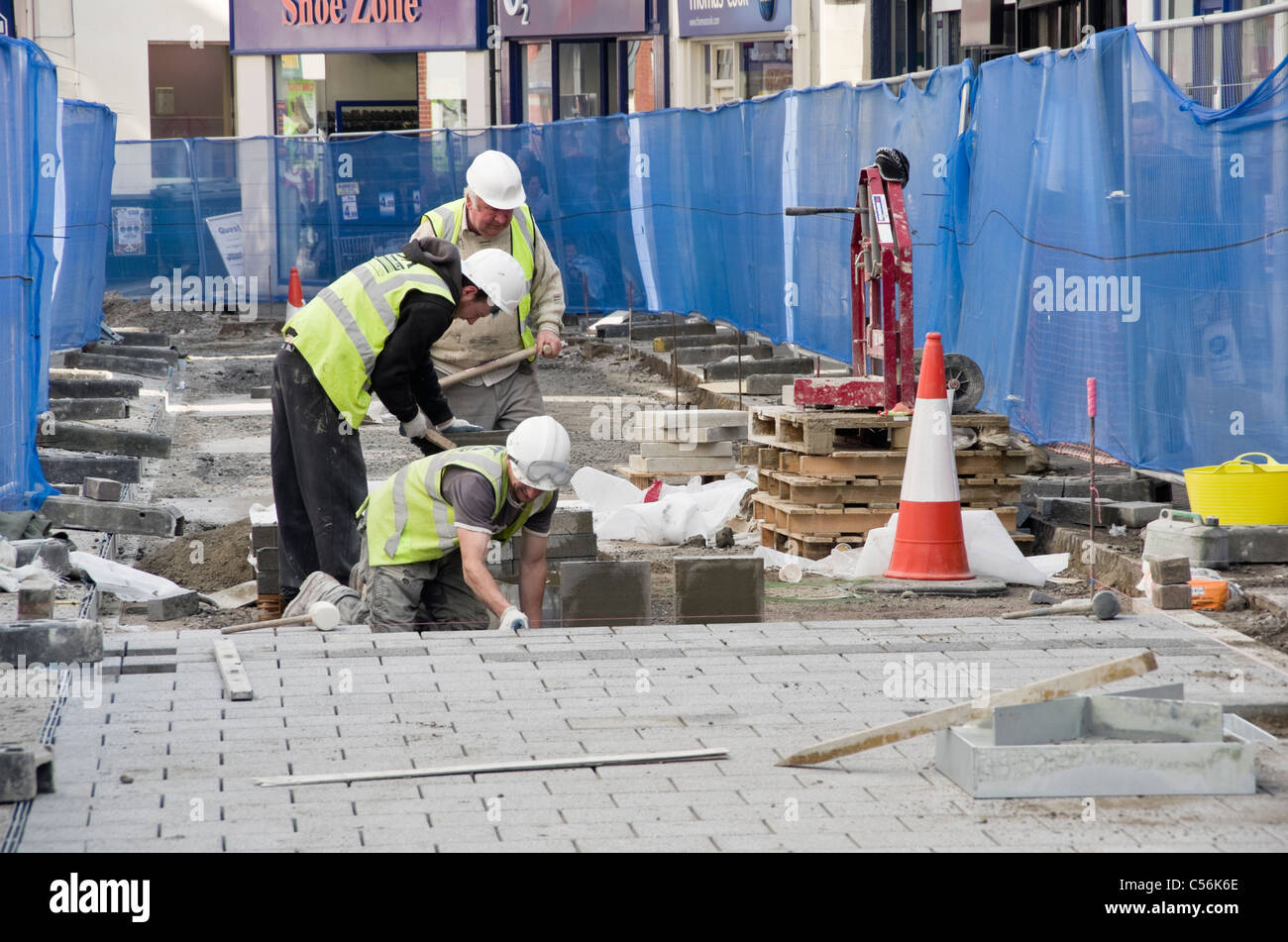 Operai del consiglio scavano la strada sostituendo le pietre di pavimentazione nel distretto. High Street, Bangor, Gwynedd, Galles del Nord, Regno Unito Foto Stock