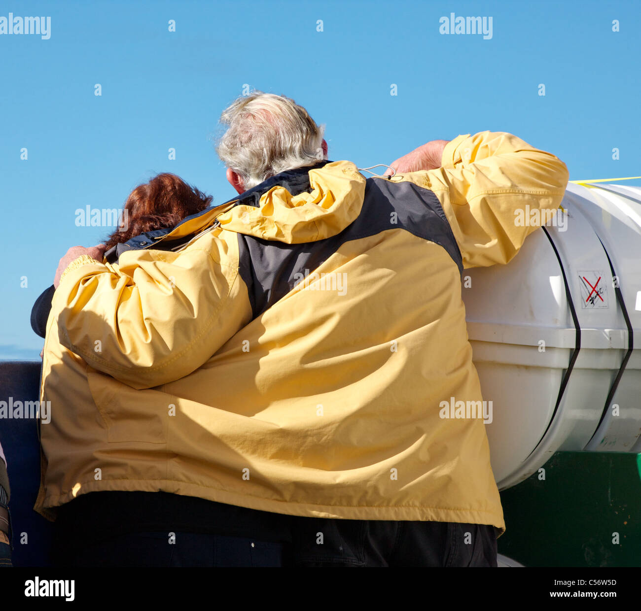Un uomo che ripara una donna dal vento utilizzando il suo mantello mentre loro sguardo fuori in mare dal ponte di una nave Foto Stock