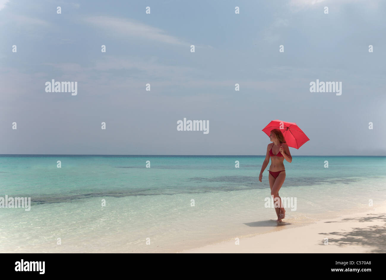 Donna che cammina con ombrellone in spiaggia Foto Stock
