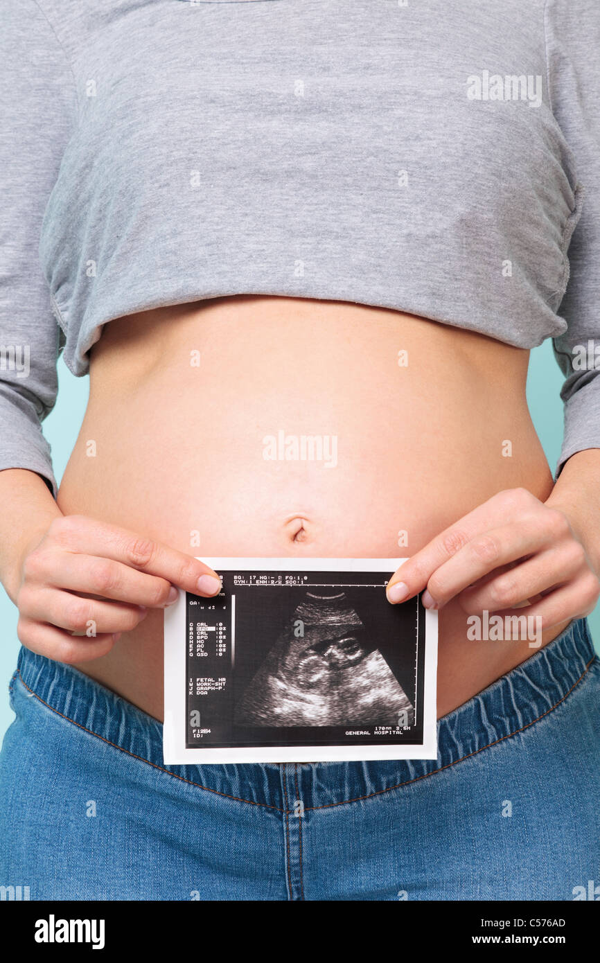 Foto di una donna in stato di gravidanza tenendo la sua scansione ad ultrasuoni contro il suo ventre. Foto Stock