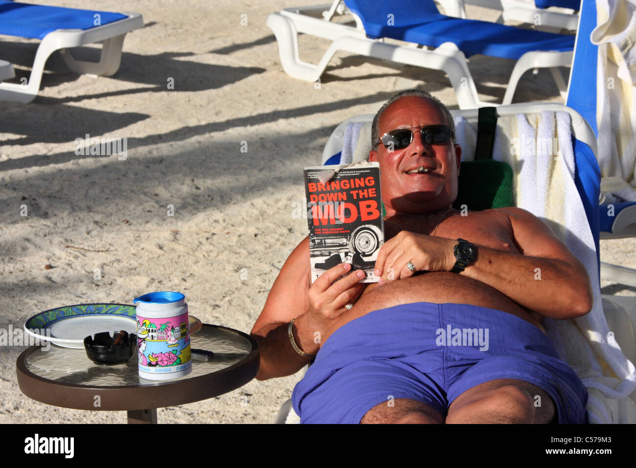Uomo di mezza età la lettura di un libro chiamato portare verso il basso la folla in una spiaggia Foto Stock