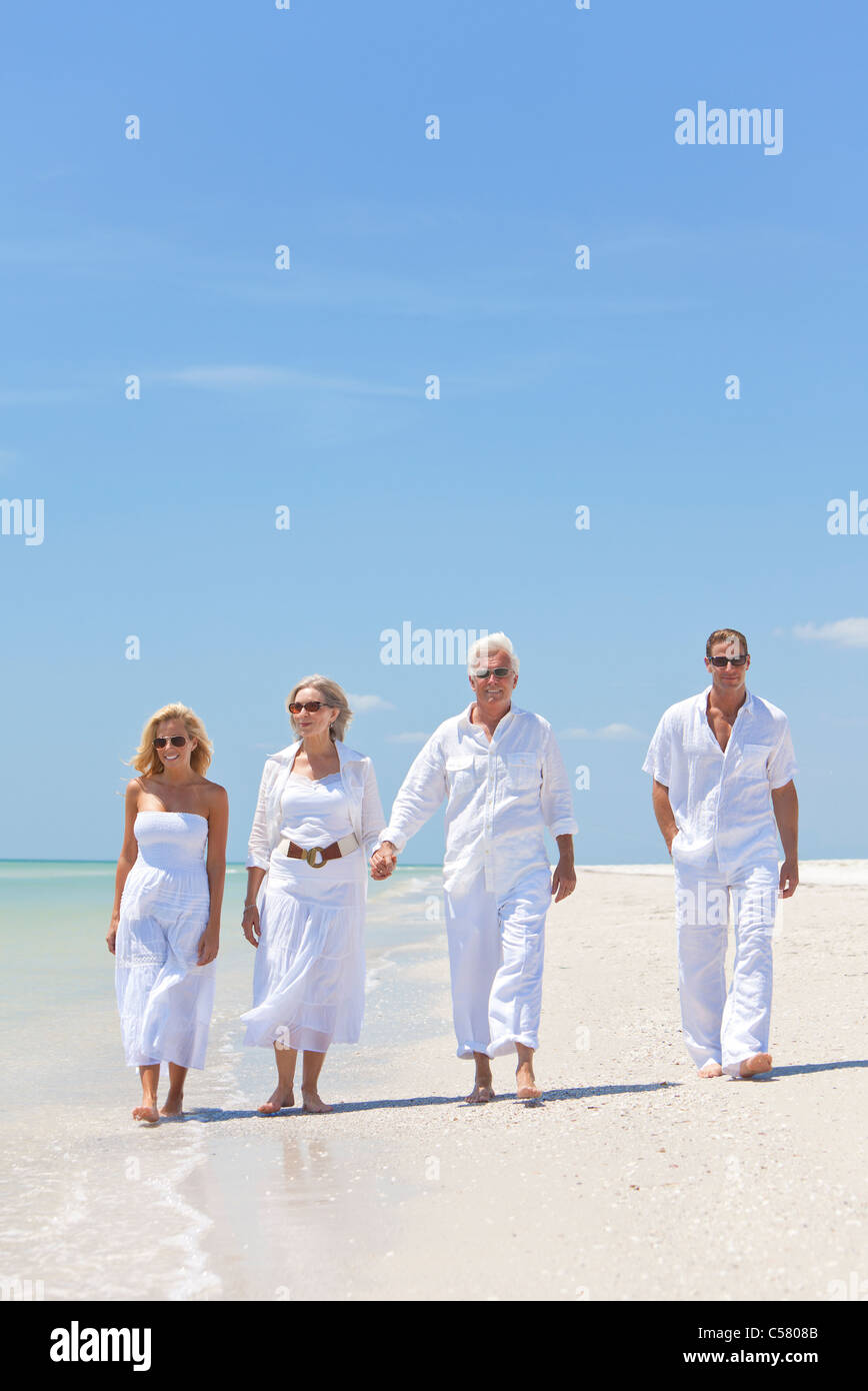 Quattro persone, due anziani, coppie o generazioni della famiglia, tenendo le mani, divertendosi e camminando su una spiaggia tropicale Foto Stock
