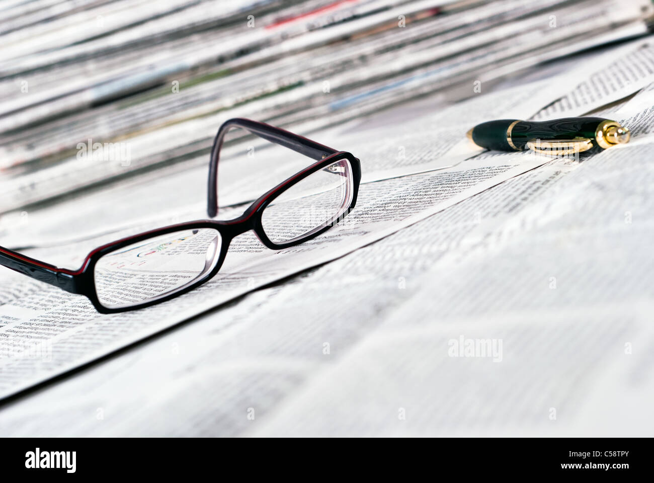 Gli occhiali da lettura e una penna a sfera giacciono su un giornale Foto Stock