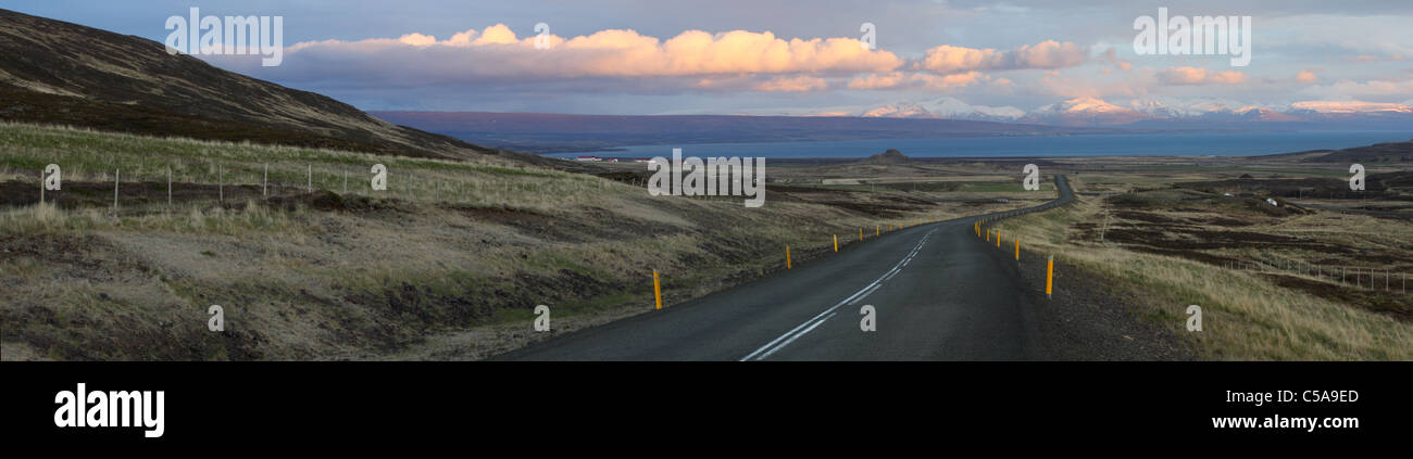 Vista panoramica della curva strada in Islanda con le montagne e le nuvole dipinte dal sole al tramonto. Foto Stock