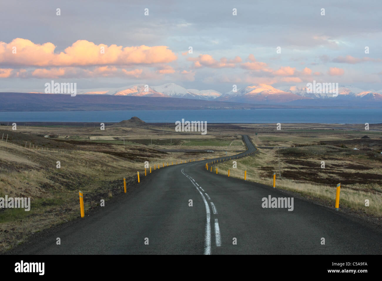 Curva strada in Islanda con le montagne e le nuvole dipinte dal sole al tramonto. Foto Stock