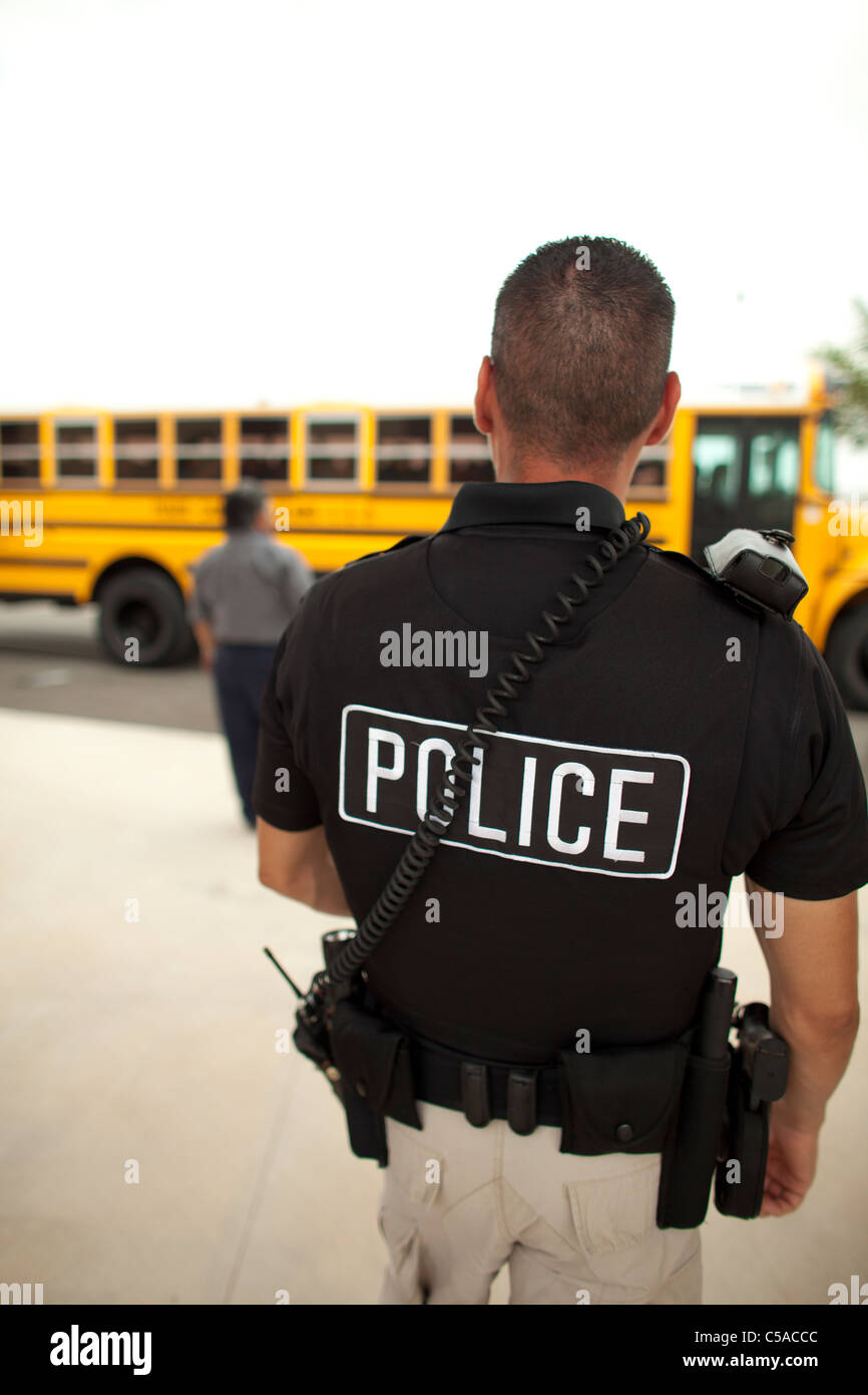 Voce maschile police officer sovrintende al bus di scuola di caricamento in corrispondenza di alta scuola in Texas del Sud Foto Stock