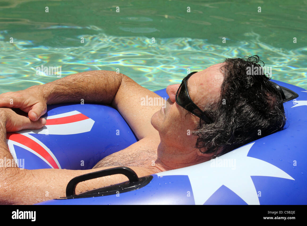 Uomo di 50 anni flottante IN UNA PISCINA IN UN ANELLO GONFIABILE BDA ORIZZONTALE Foto Stock