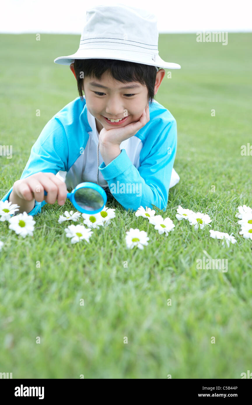 Ragazzo disteso sul prato con lente di ingrandimento in mano Foto Stock