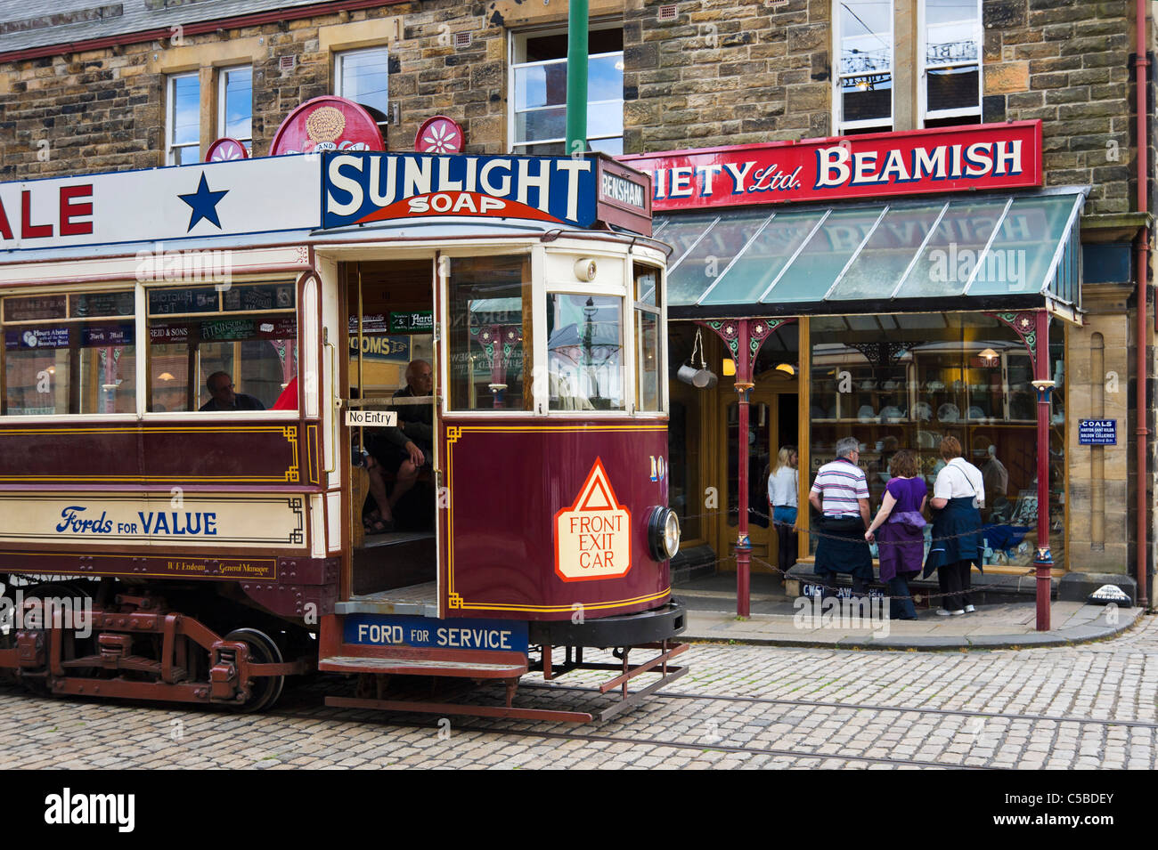 Vecchio tram di fronte a negozi di High Street nella città, Beamish Open Air Museum, County Durham, North East England, Regno Unito Foto Stock