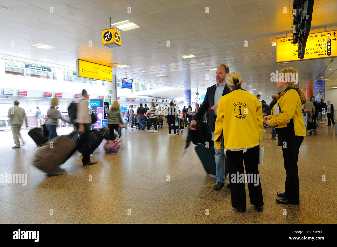 Informazioni sull'aeroporto personale che indossa Giacche gialle vicino ai banchi di check-in area partenze dell'aeroporto internazionale di Glasgow (GLA) foto di scorta della Scozia Foto Stock