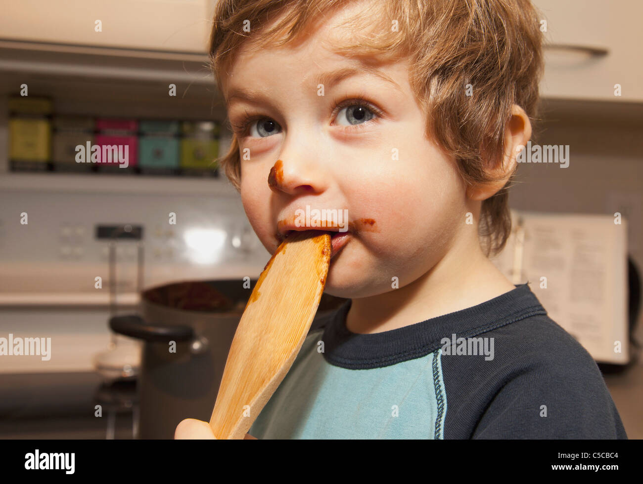 Un ragazzo che lambisce un cucchiaio di cioccolato sul suo volto; Langley, British Columbia, Canada Foto Stock