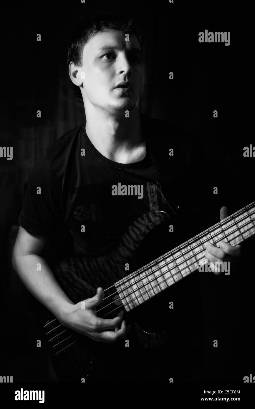 Giovane musicista con chitarra basso, in piedi su un sfondo nero Foto Stock