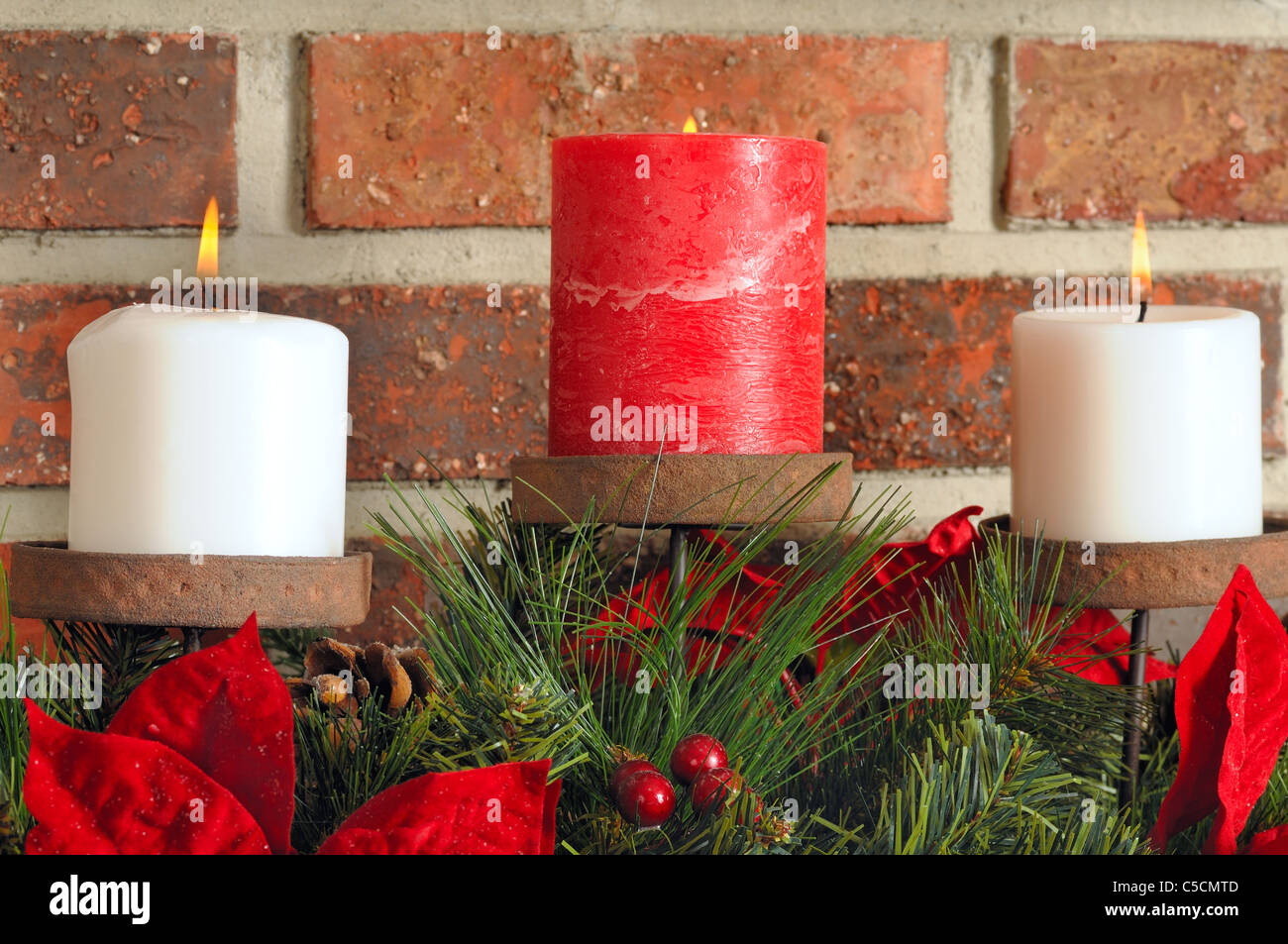 Tre candele di Natale su sempreverdi e poinsettia con un sfondo mattone Foto Stock