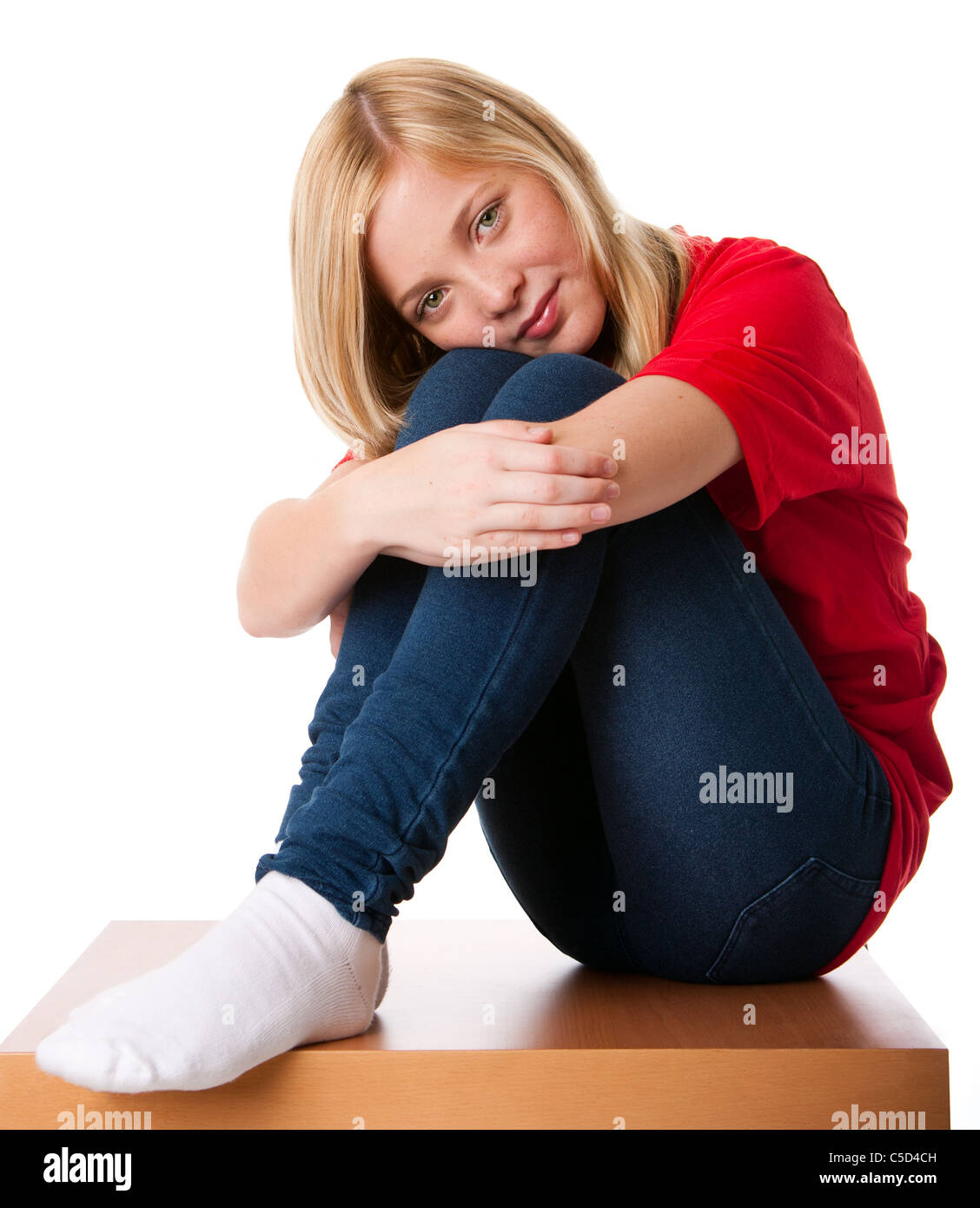 Carina ragazza adolescente sentirsi soli seduto da solo con le ginocchia tirato verso l'alto e le braccia intorno alle gambe, isolata. Foto Stock