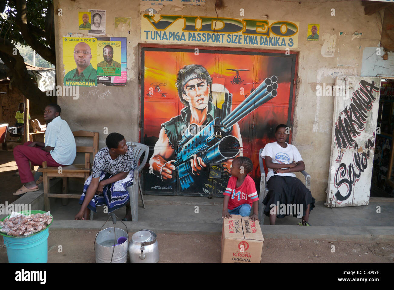 TANZANIA Street scene n Mabitini, Mwanza. Esterno del piccolo negozio con il murale sulla porta raffigurante Rambo. fotografia di Sean Sprague Foto Stock