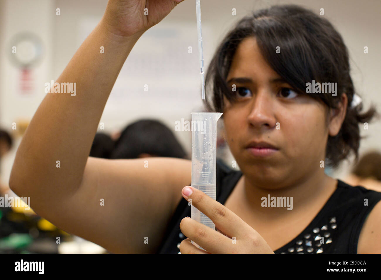 Femmina ispanica di alta scuola studente utilizza un contagocce per misurare liquido in un cilindro graduato in high school science lab class Foto Stock