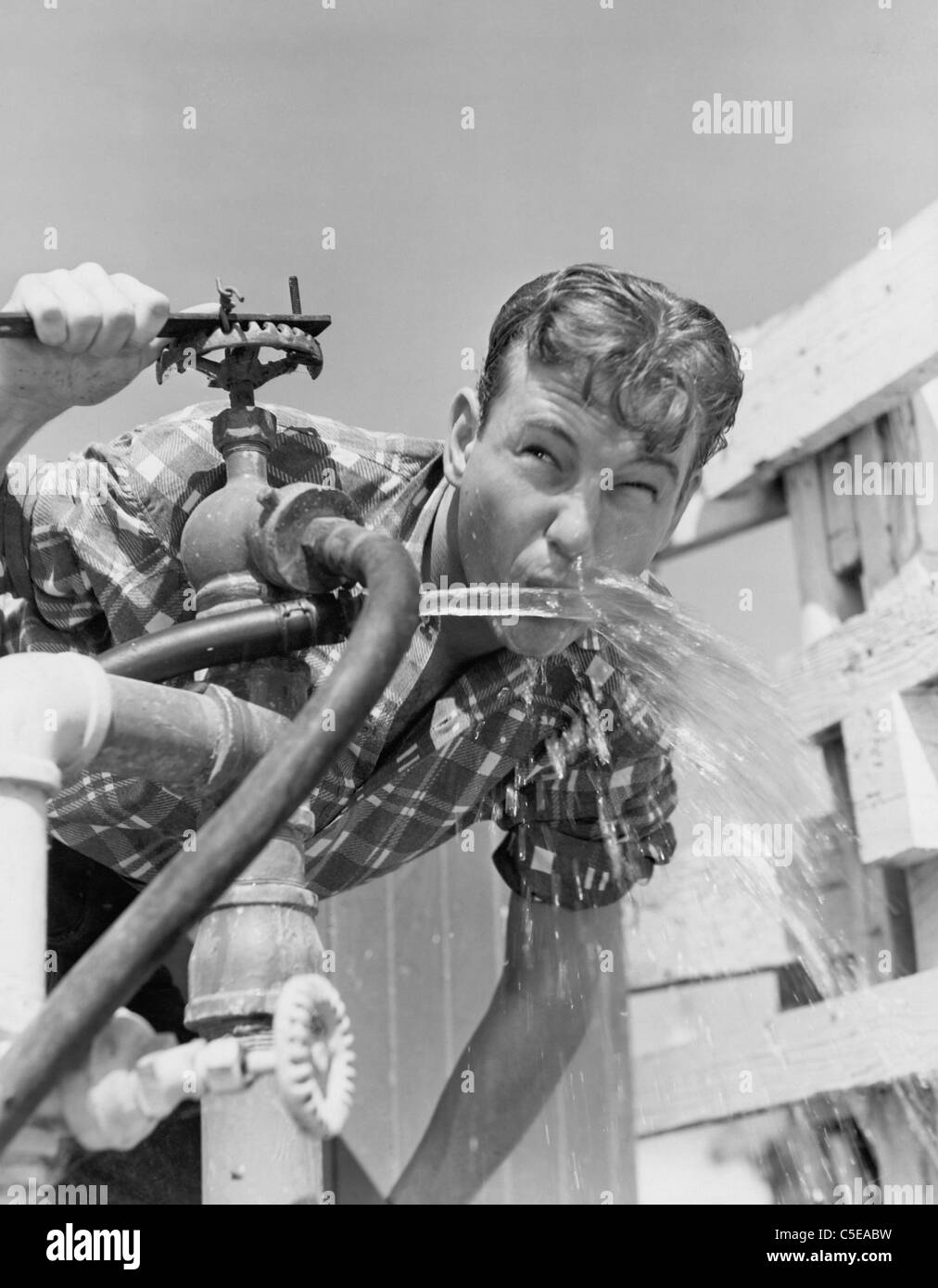 Giovane uomo di bere acqua dal tubo flessibile Foto Stock