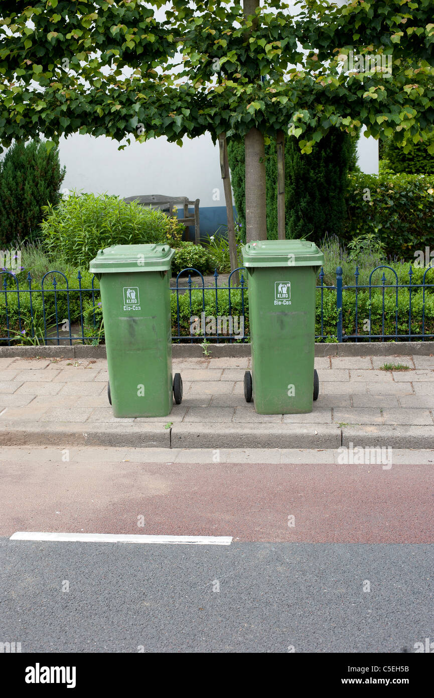 Due verde biologico di riciclaggio dei contenitori per i rifiuti sul marciapiede davanti a un albero Foto Stock