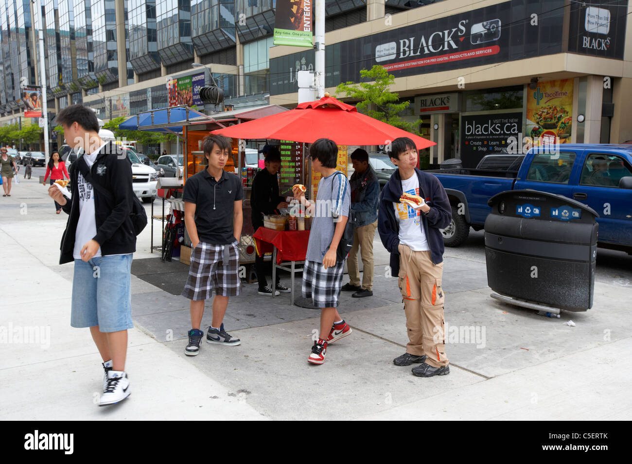 Un gruppo di giovani uomini asiatici mangiare hotdog comprato da sulla strada di hot dog vendor Downtown Toronto Ontario Canada Foto Stock