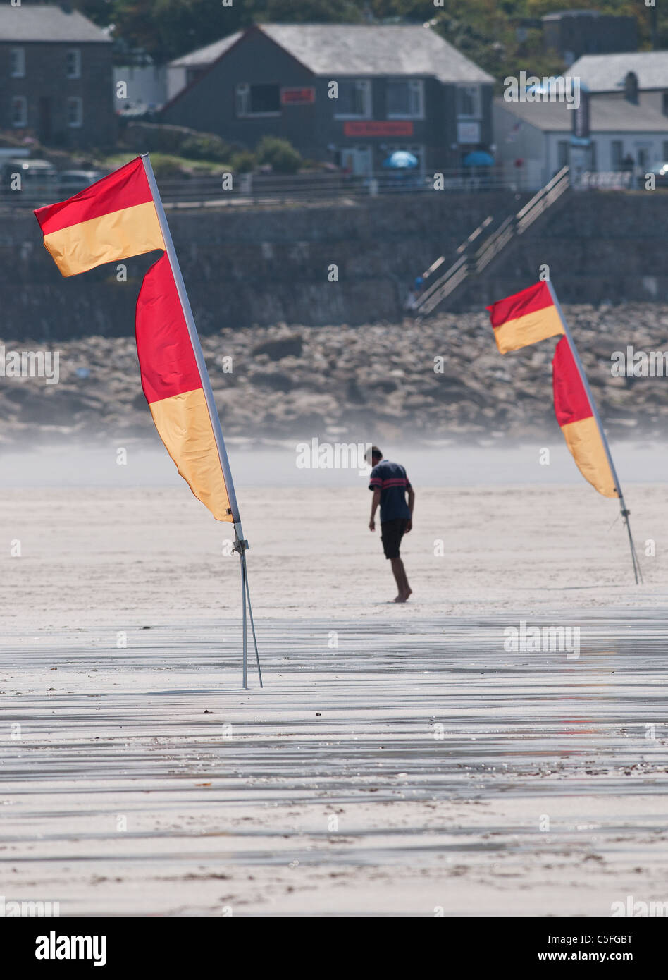 Un uomo che cammina tra due piscina bandiere di sicurezza sulla spiaggia di Sennen. Foto Stock