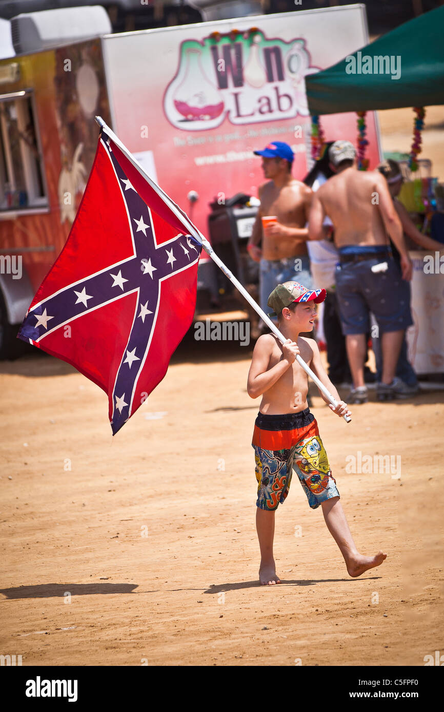 Ragazzo giovane cammina con una bandiera confederato durante la stagione estiva con Redneck Games Dublino, GA. Foto Stock