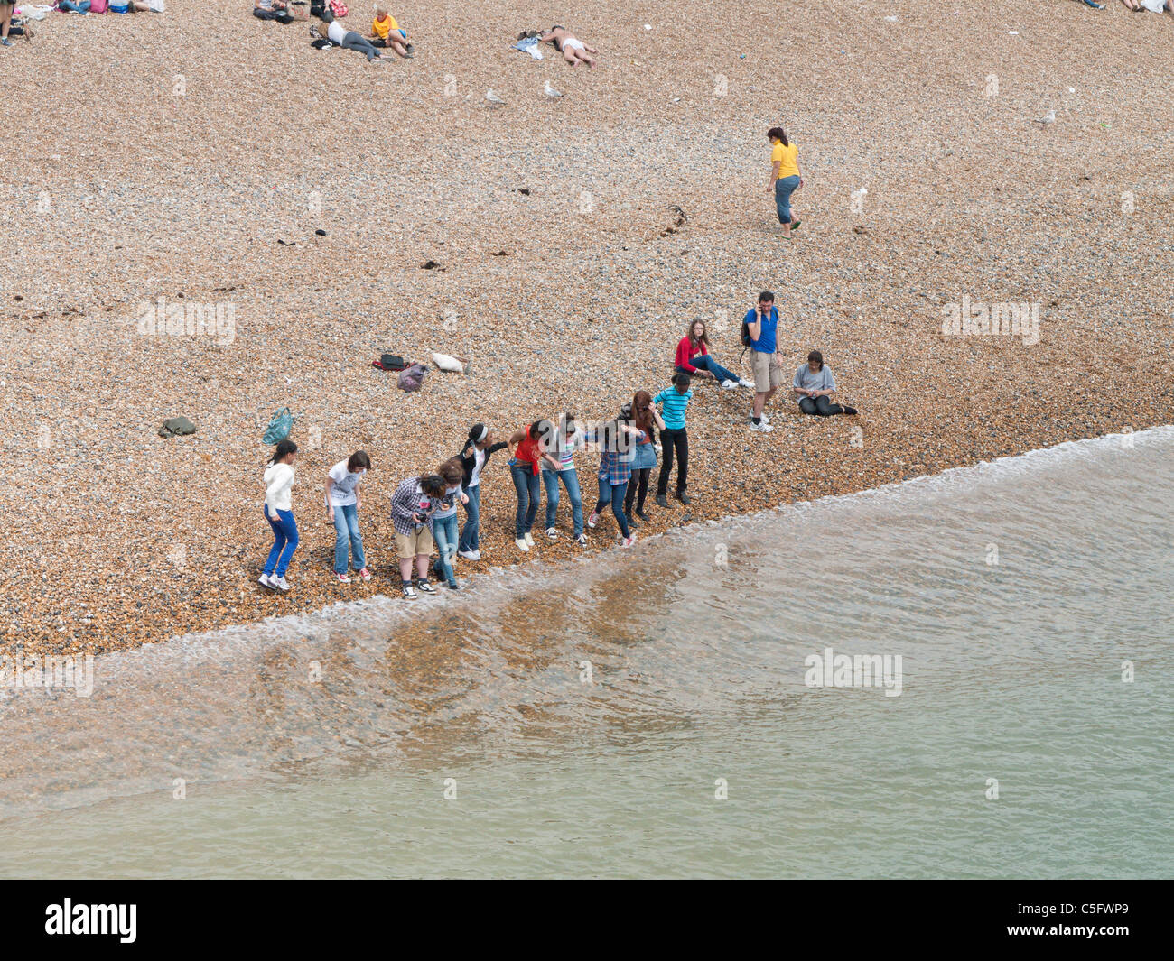 Una linea di studenti stranieri coraggioso il waveson la spiaggia di Brighton, Sussex, Inghilterra Foto Stock