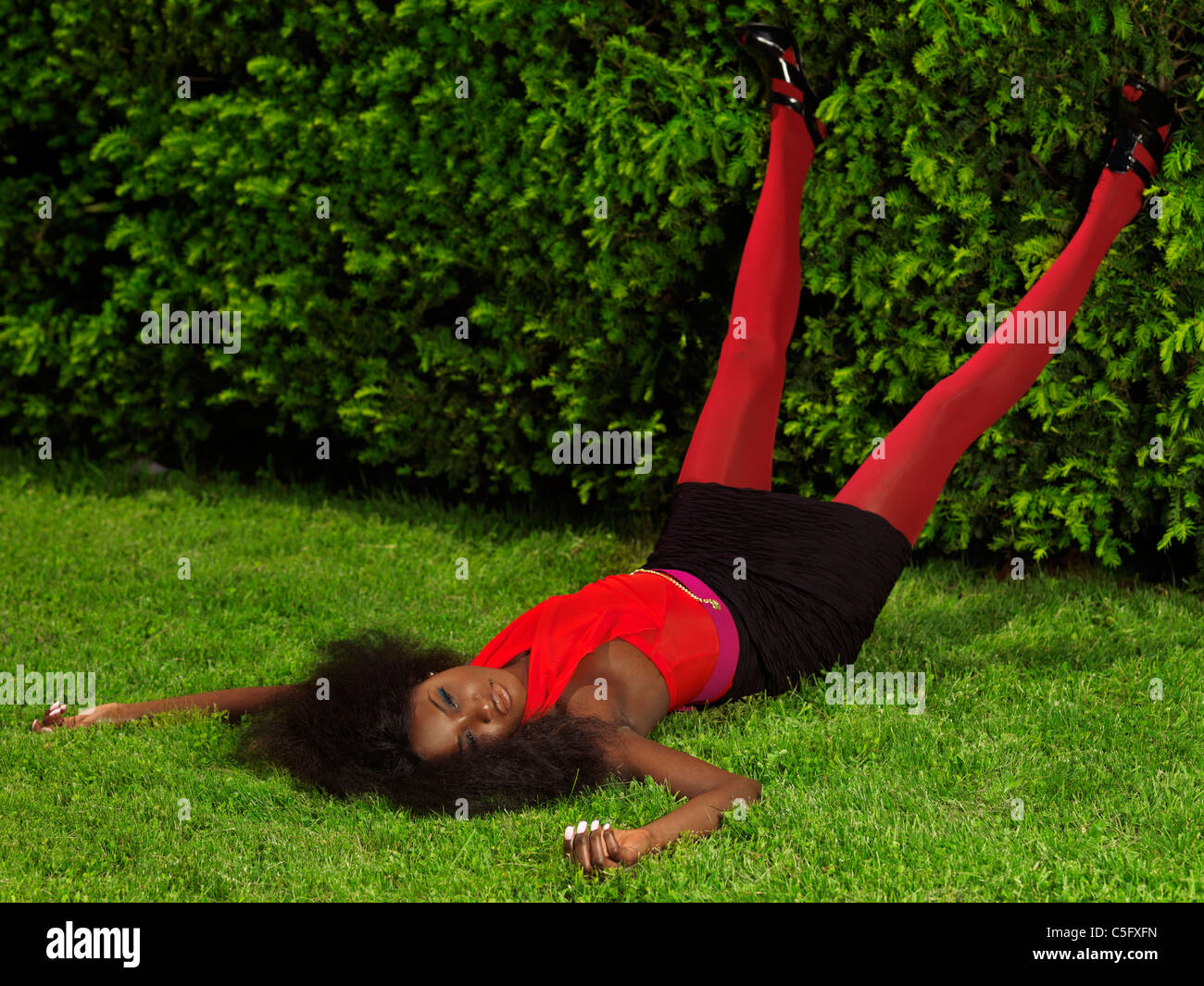 Licenza disponibile presso MaximImages.com giovane donna nera elegante con eleganti abiti luminosi sdraiati sull'erba di un parco Foto Stock