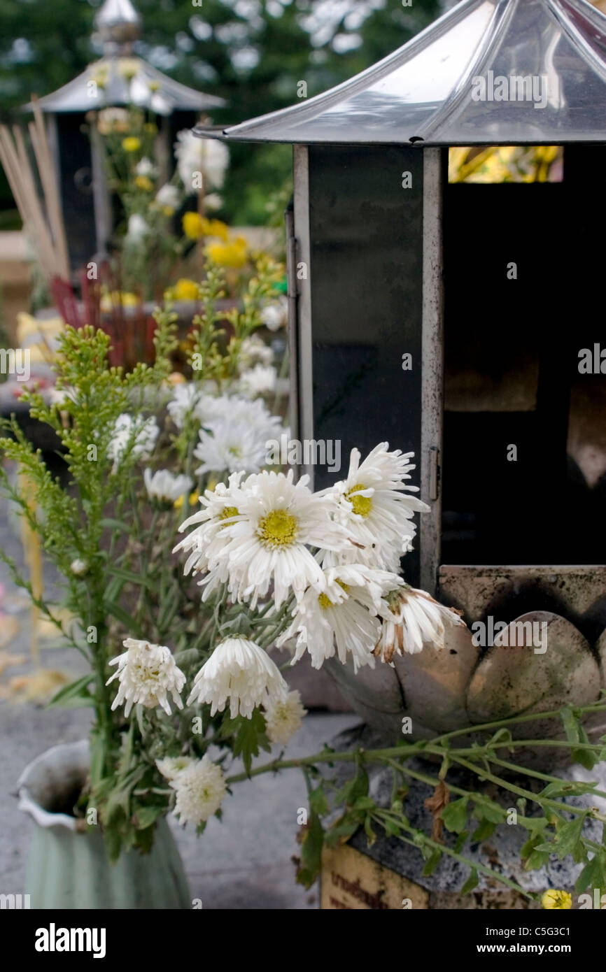 Fiori, lanterne e altri oggetti formano un altare esterno visualizzazione in un tempio buddista in Thailandia del Nord. Foto Stock