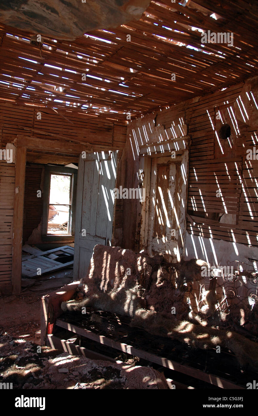 Un vecchio divano è illuminata dalla luce del sole che splende attraverso un parzialmente assente il tetto di una casa nella città fantasma di Cuervo, Nuovo Messico. Foto Stock