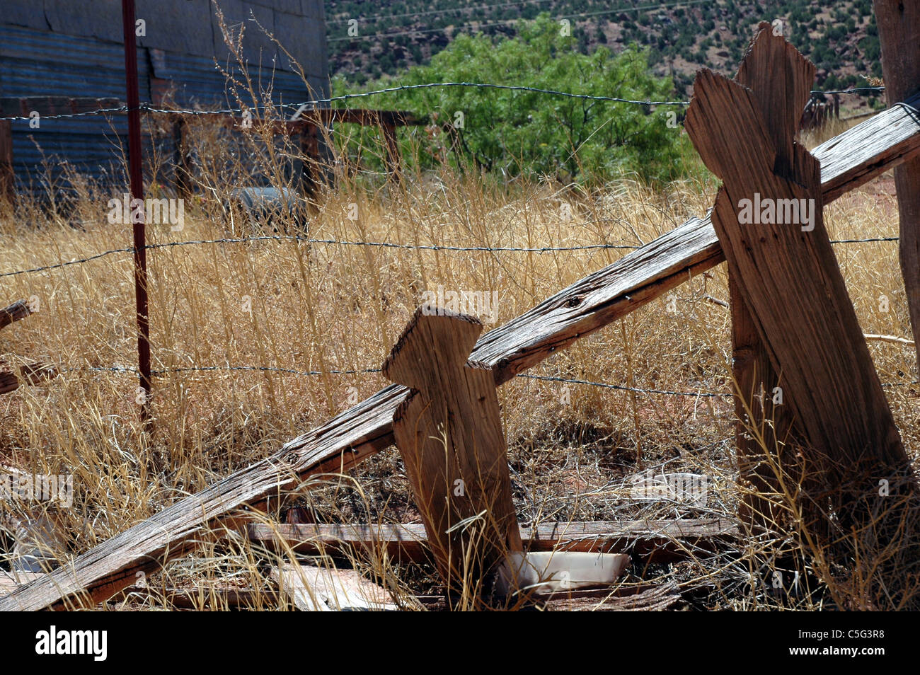 Le stecche di un Picket Fence cadono verso il basso dietro il più moderno Filo spinato in quella parzialmente abbandonato città di Cuervo, Nuovo Messico. Foto Stock