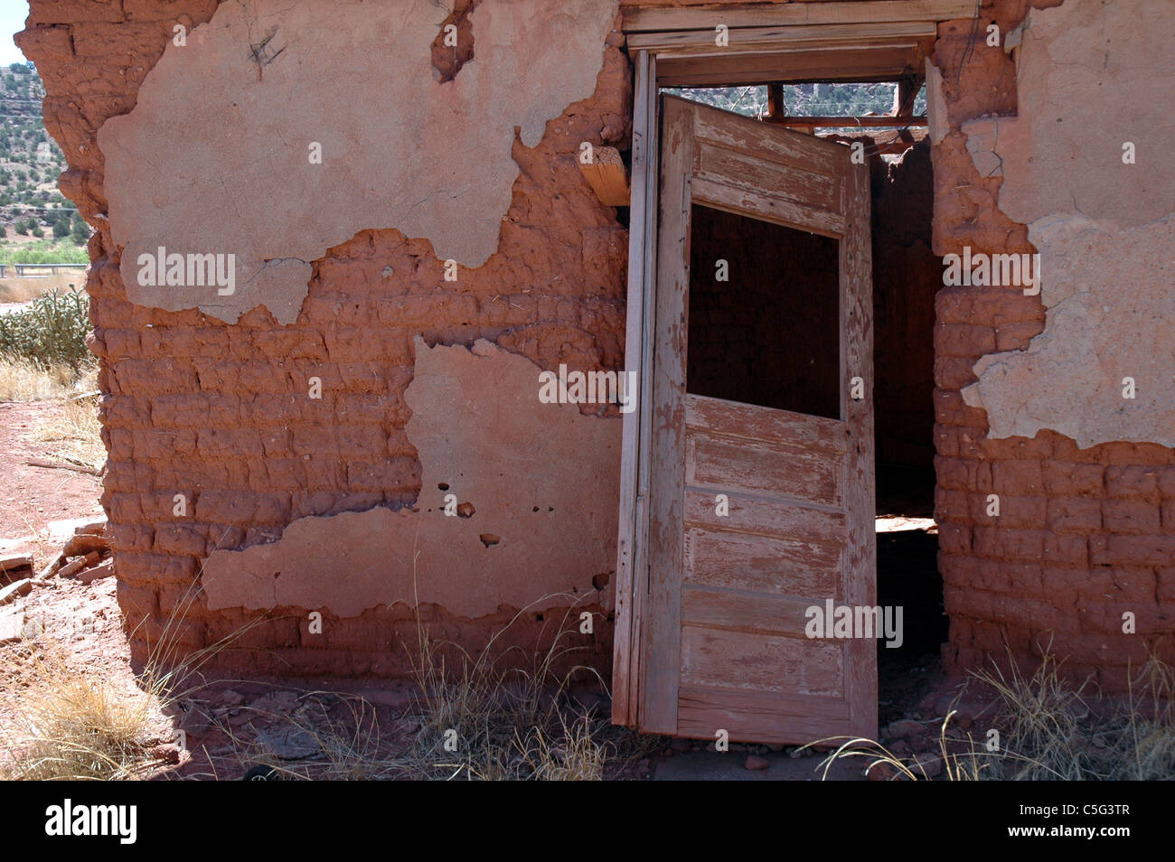Una porta si inclina verso l'interno su una casa abbandonata in Cuervo, Nuovo Messico. Il mattone di fango sotto il cracking adobe facciata è visibile. Foto Stock