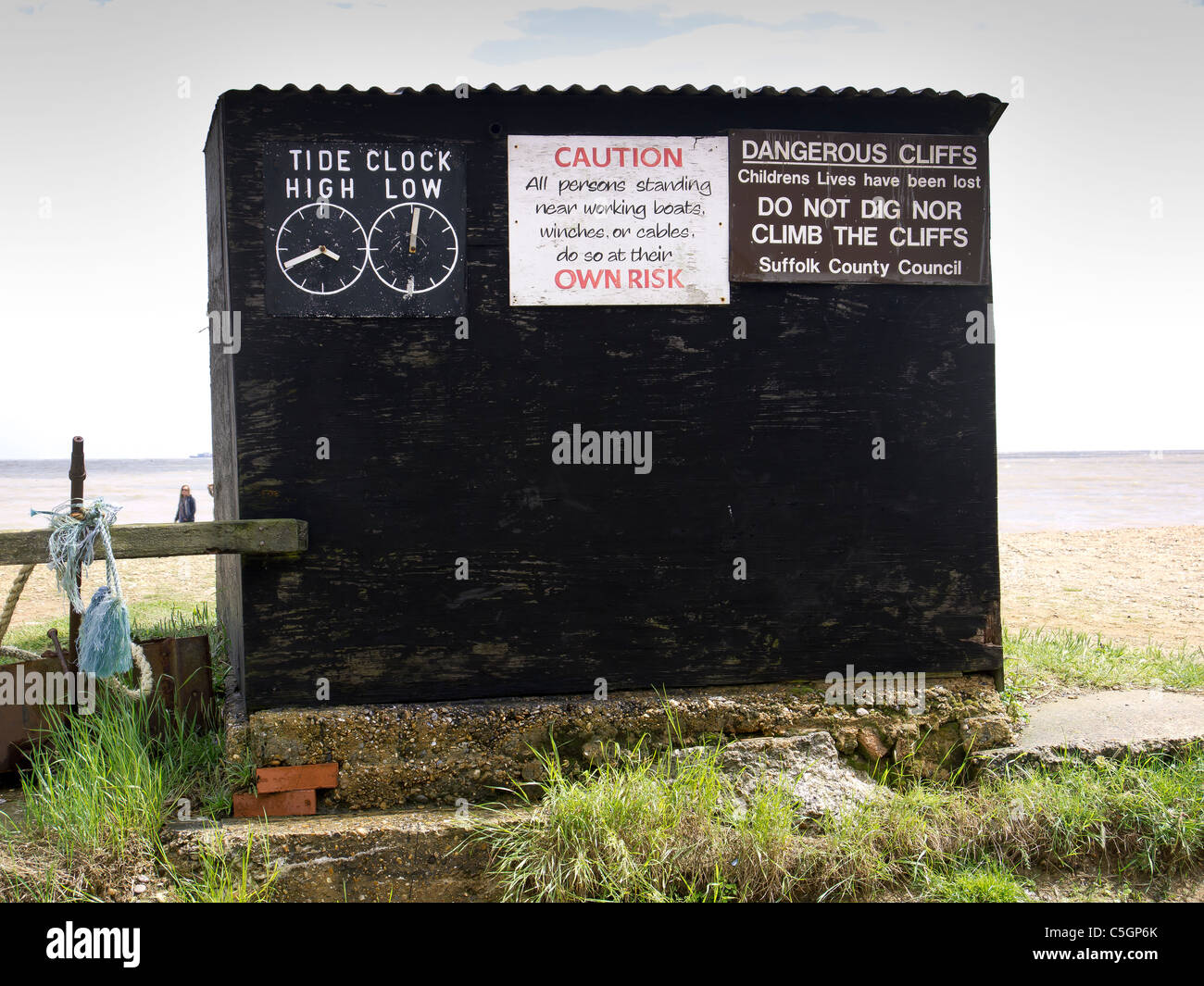 Un asfalto nero Fisherman's capanna sulla spiaggia di Dunwich con orari delle maree e avvisi di pericolo Foto Stock