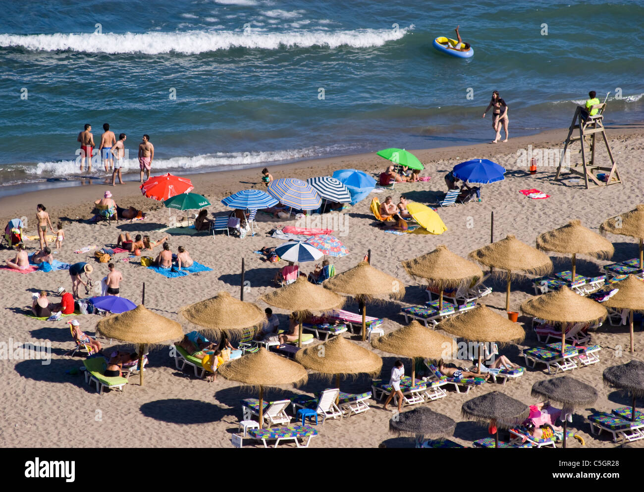 Vacanzieri godere il mare e la sabbia sotto gli ombrelloni sulla spiaggia di Fuengirola COSTA DEL SOL sorvegliata da un bagnino Foto Stock