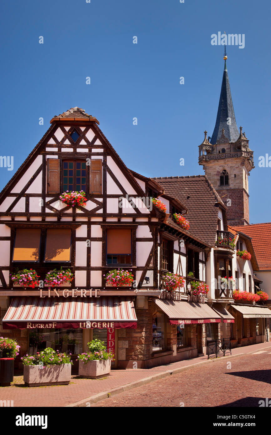 I negozi lungo la Rue Saint Odile con torre di Hotel de Ville oltre, Obernai Alsazia Bas-Rhin Francia Foto Stock