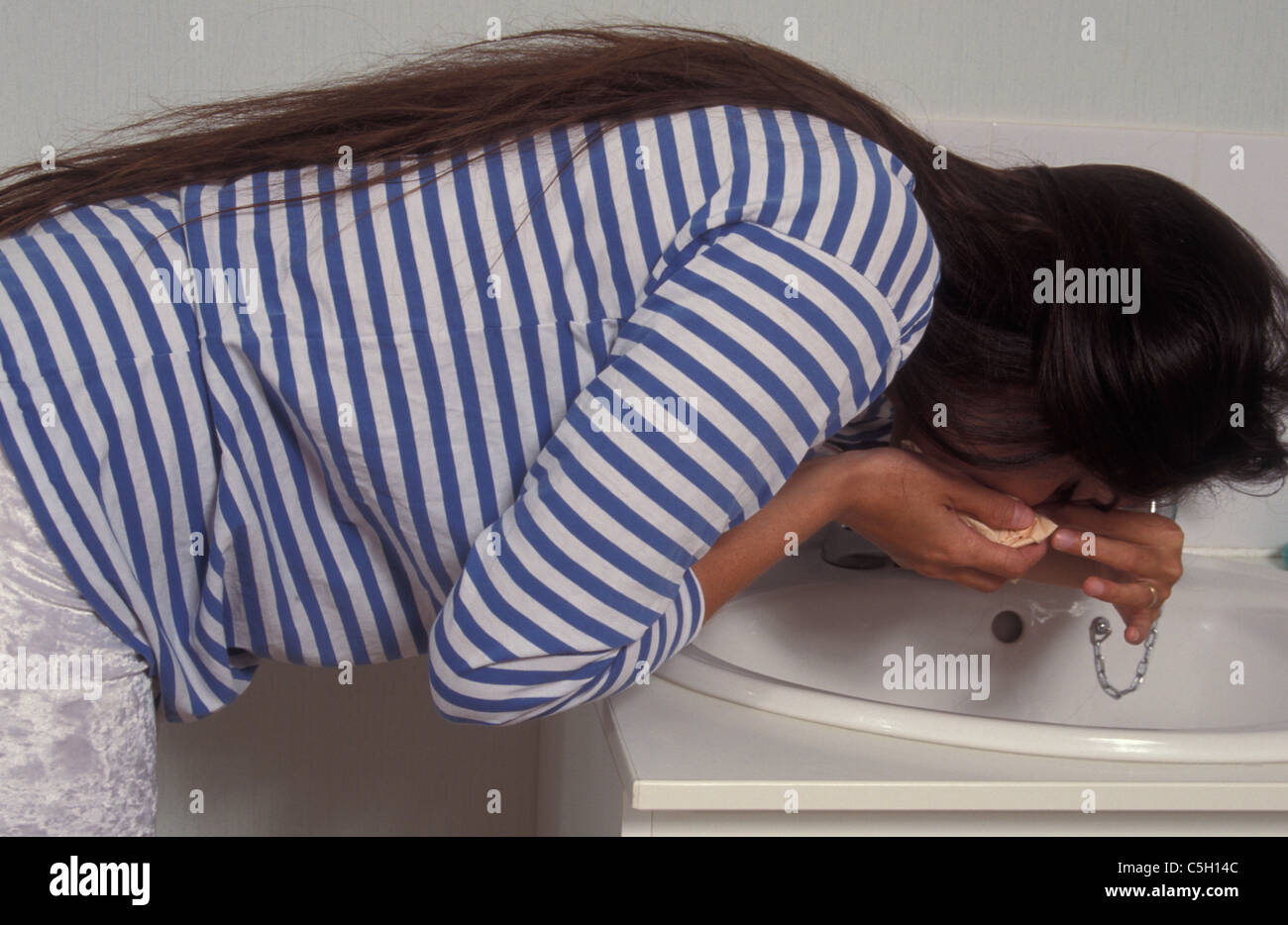 Donna in gravidanza affette da naso spurgare la piegatura su lavandino Foto Stock