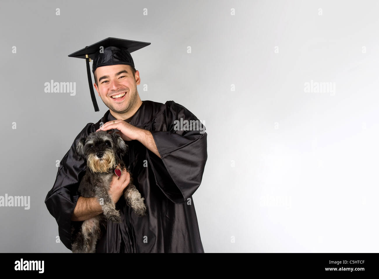 Un recente collegio o diplomato nel suo cappello e camice tenendo il suo cane nelle sue braccia. Foto Stock