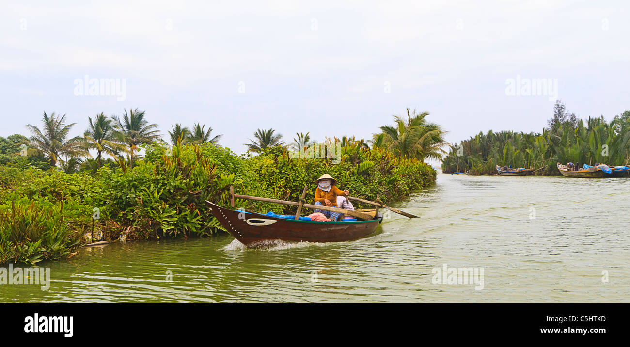 Donna locale righe la sua strada verso il basso Thu Bon fiume in barca tradizionale, Hoi An, Vietnam centrale. Foto Stock