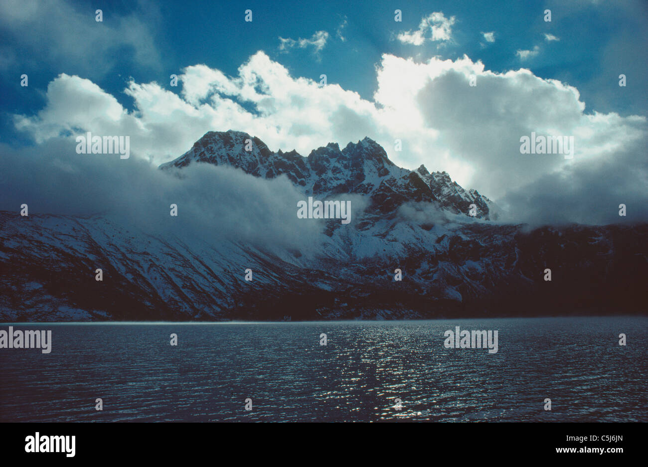 Frastagliate in stile alpino picchi e soleggiato pomeriggio nuvole riflettono in tutta l'acqua scintillante di un lago glaciale a Gokyo, Khumbu Foto Stock