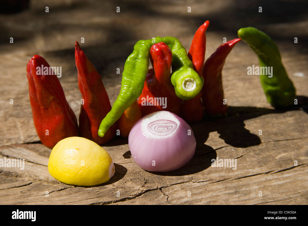 Grani di pepe rosso e il pepe verde, una cipolla e un quarto di un limone sul tavolo di legno Foto Stock