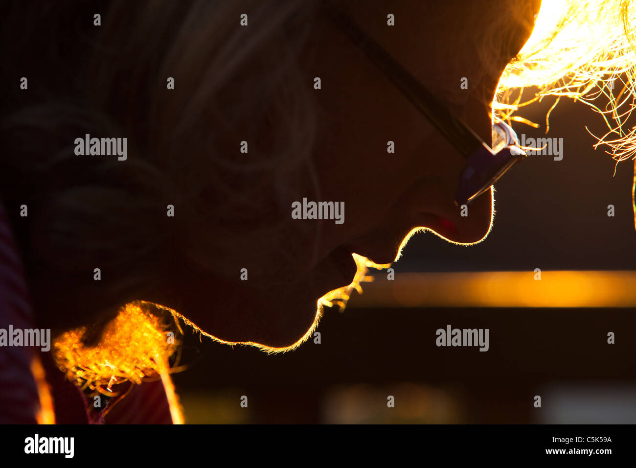 Una donna di mezza età che indossa gli occhiali da lettura è illuminato dal sole al tramonto. Foto Stock