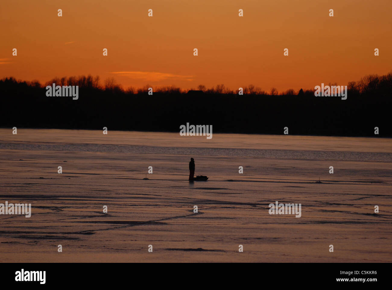 Con le Montagne Adirondack in background, un pescatore di ghiaccio si erge sul ghiaccio mentre la pesca sul lago Champlain nel Vermont Foto Stock