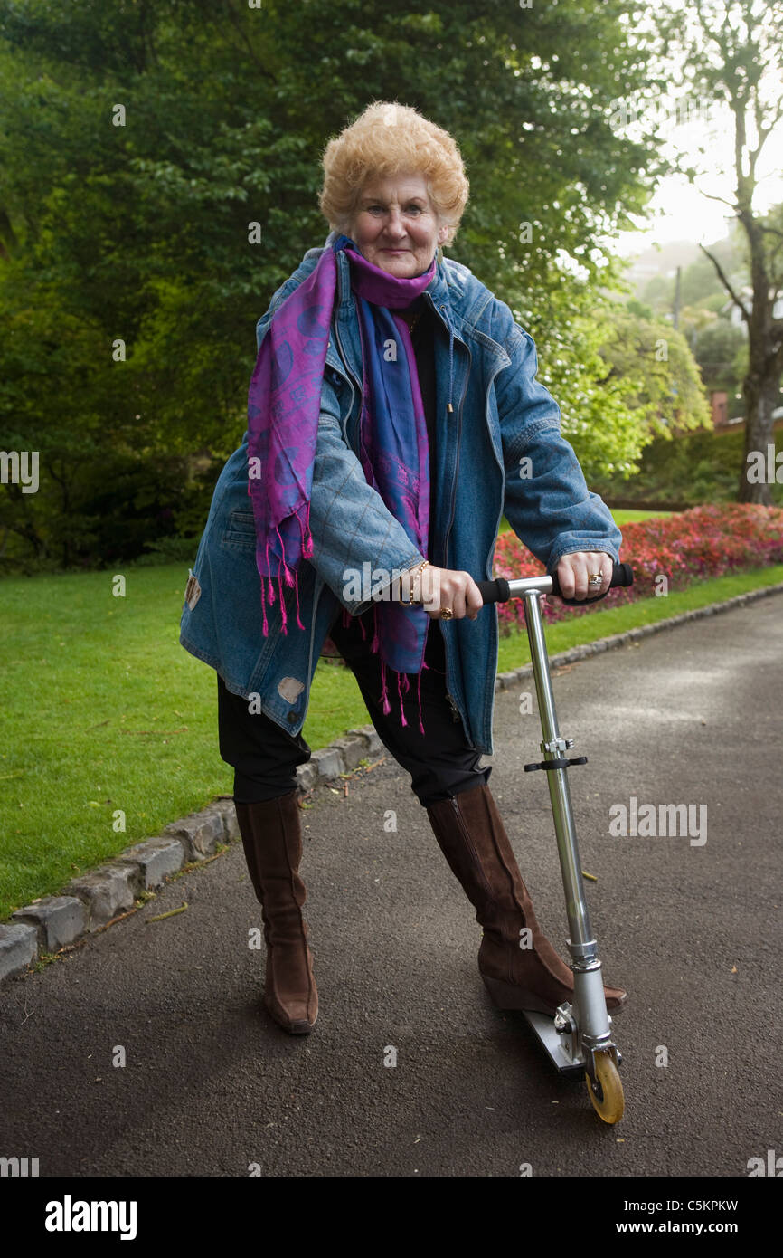 Una donna nel suo 60s in piedi con un piede-scooter in un giardino pubblico, Nuova Zelanda Foto Stock