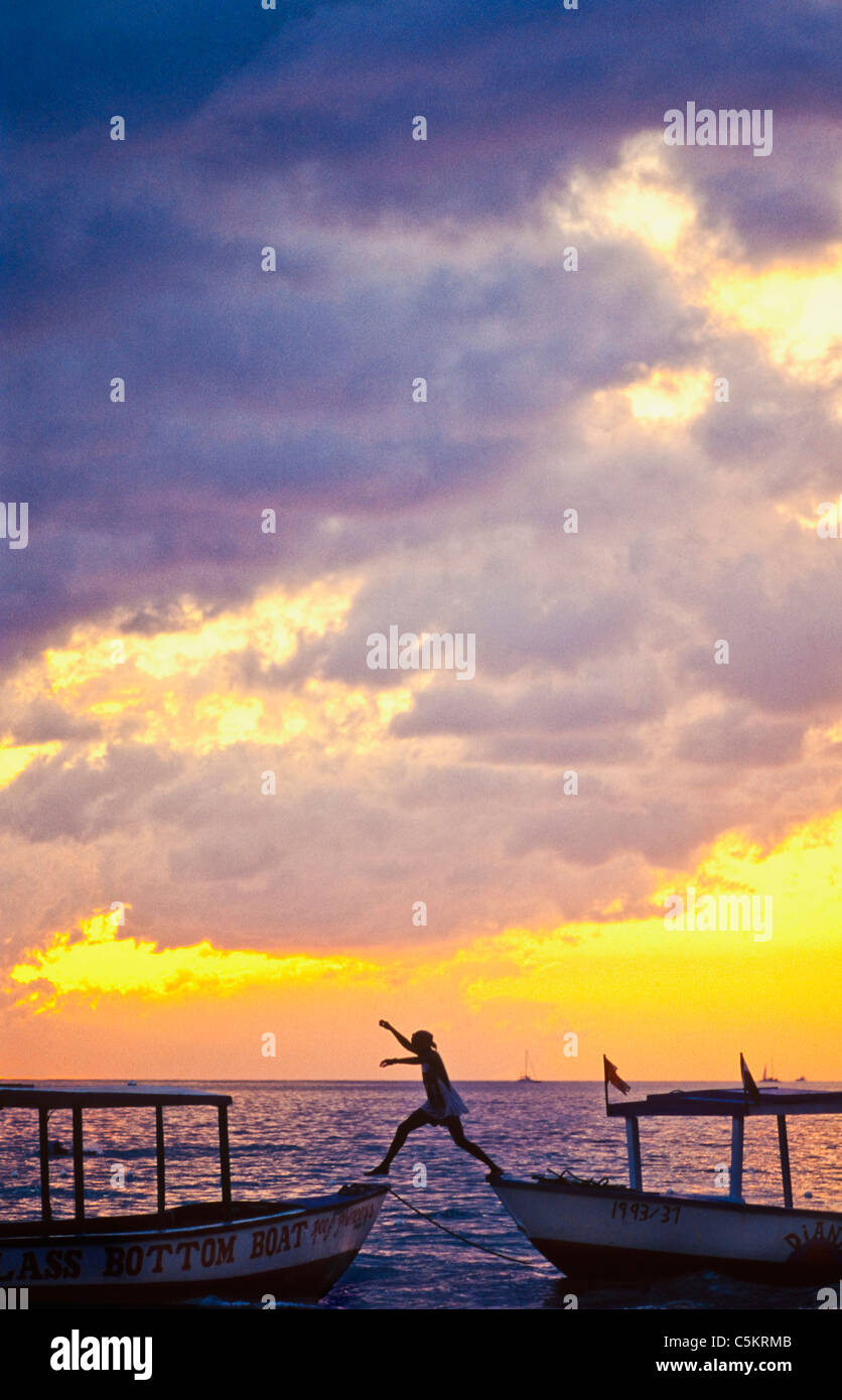 Ragazzo in Giamaica salta da una barca per un altro colpo contro un tramonto di Negril. Foto Stock